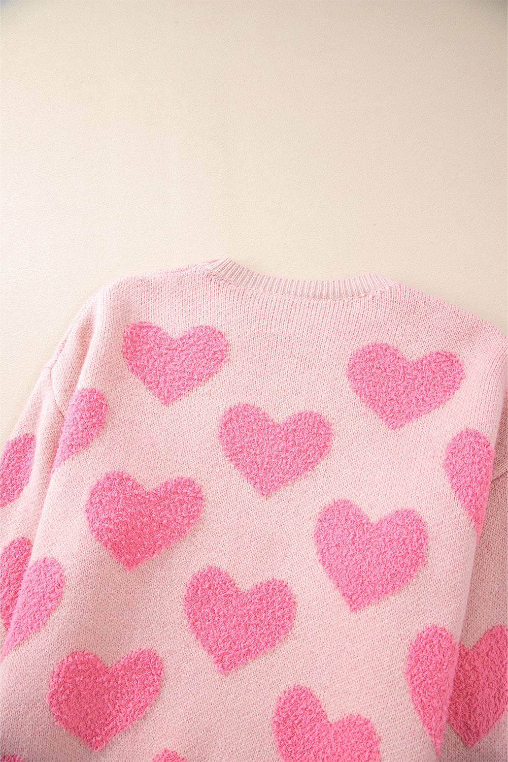 Blush pink knit sweater with textured heart pattern and crew neck.