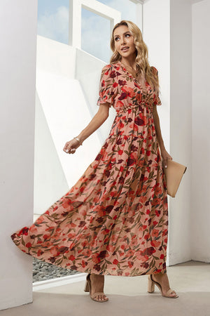 Tiered floral maxi dress with puff sleeves and a ruffled neckline in a blush pink with red and burgundy blossoms.