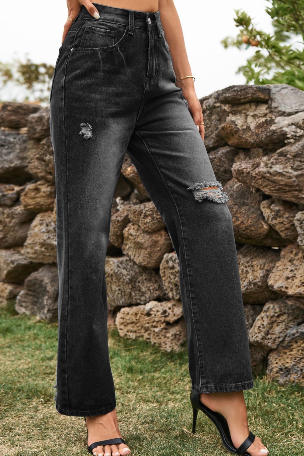 Distressed dark wide-leg denim trousers with ripped details and a button closure.