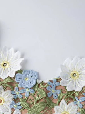 Embroidered floral maxi dress detail with white and blue appliquéd flowers and green leaves.