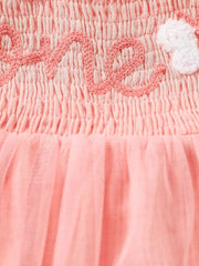 Apricot smocked baby bodysuit with embroidered "love" and a white heart detail, and a tulle skirt.