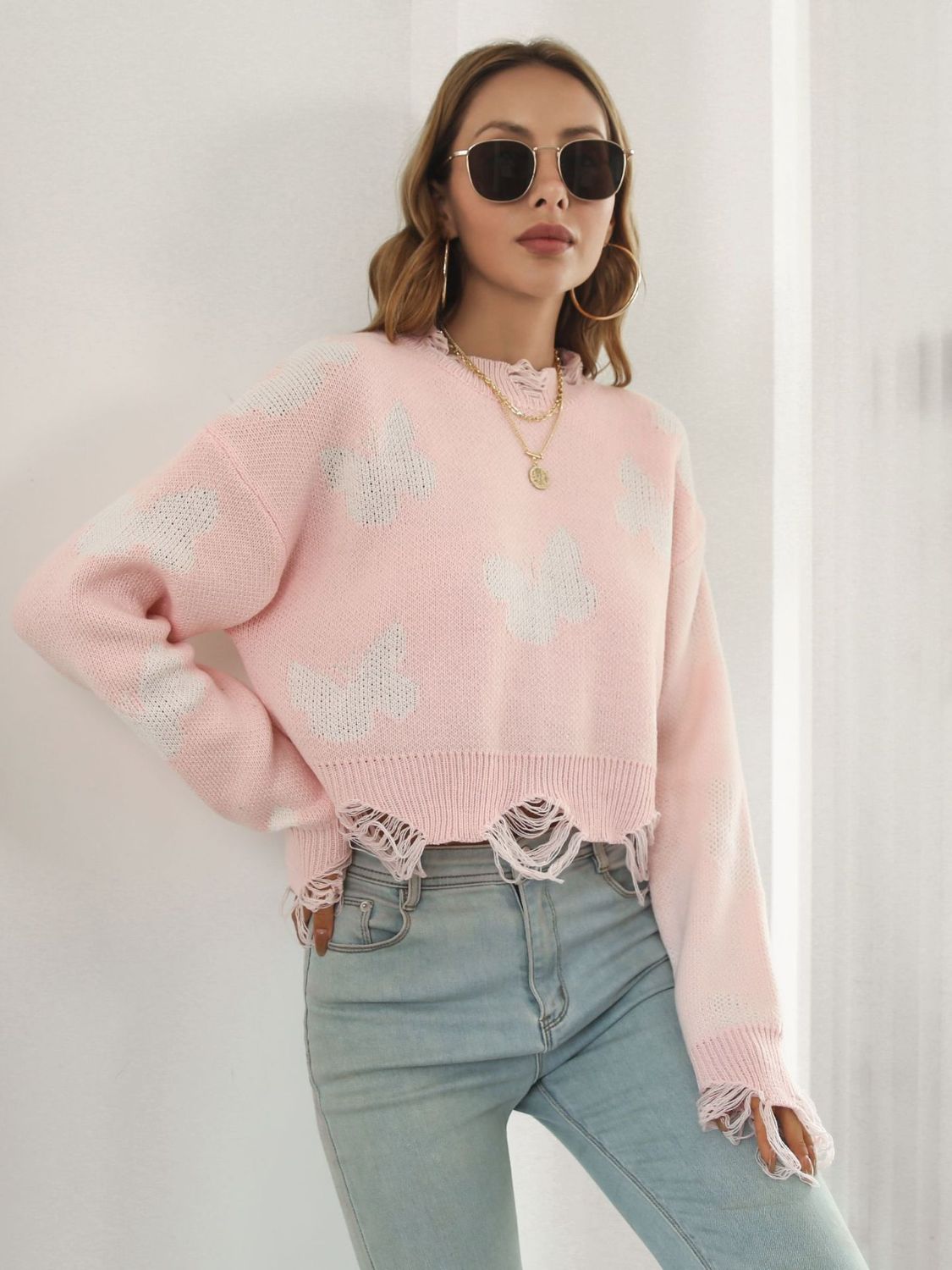 Blush pink cropped knit sweater with distressed butterfly print and frayed hem.