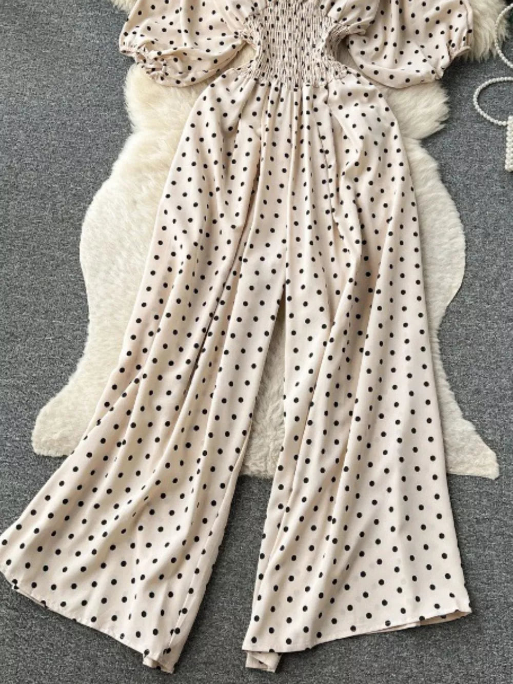 Beige polka dot smocked wide-leg romper with puff sleeves.