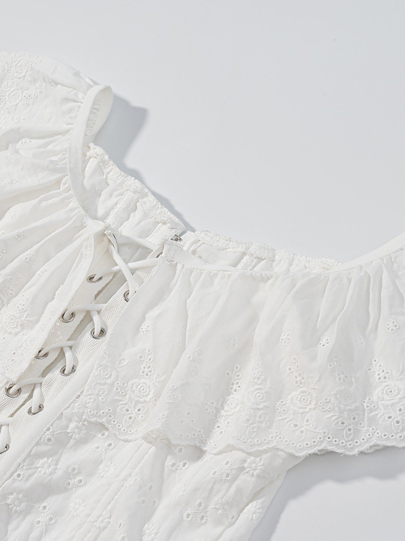White eyelet lace-up corset tank top with ruffle trim and delicate floral embroidery.