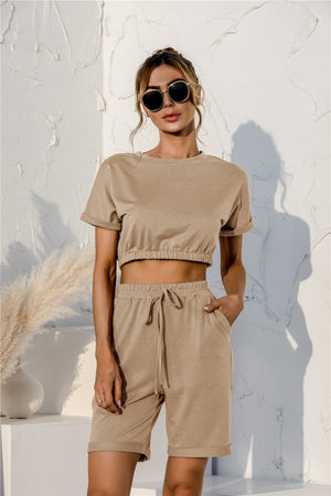 Tan loungewear set with cropped t-shirt and drawstring shorts, featuring rolled sleeves and elastic waistband.