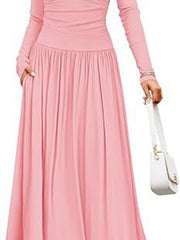 Pink ruched maxi dress with long sleeves and pockets, styled with a white handbag.