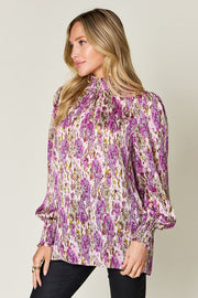 High neck abstract print blouse in red-violet with long sleeves and smocked cuffs.