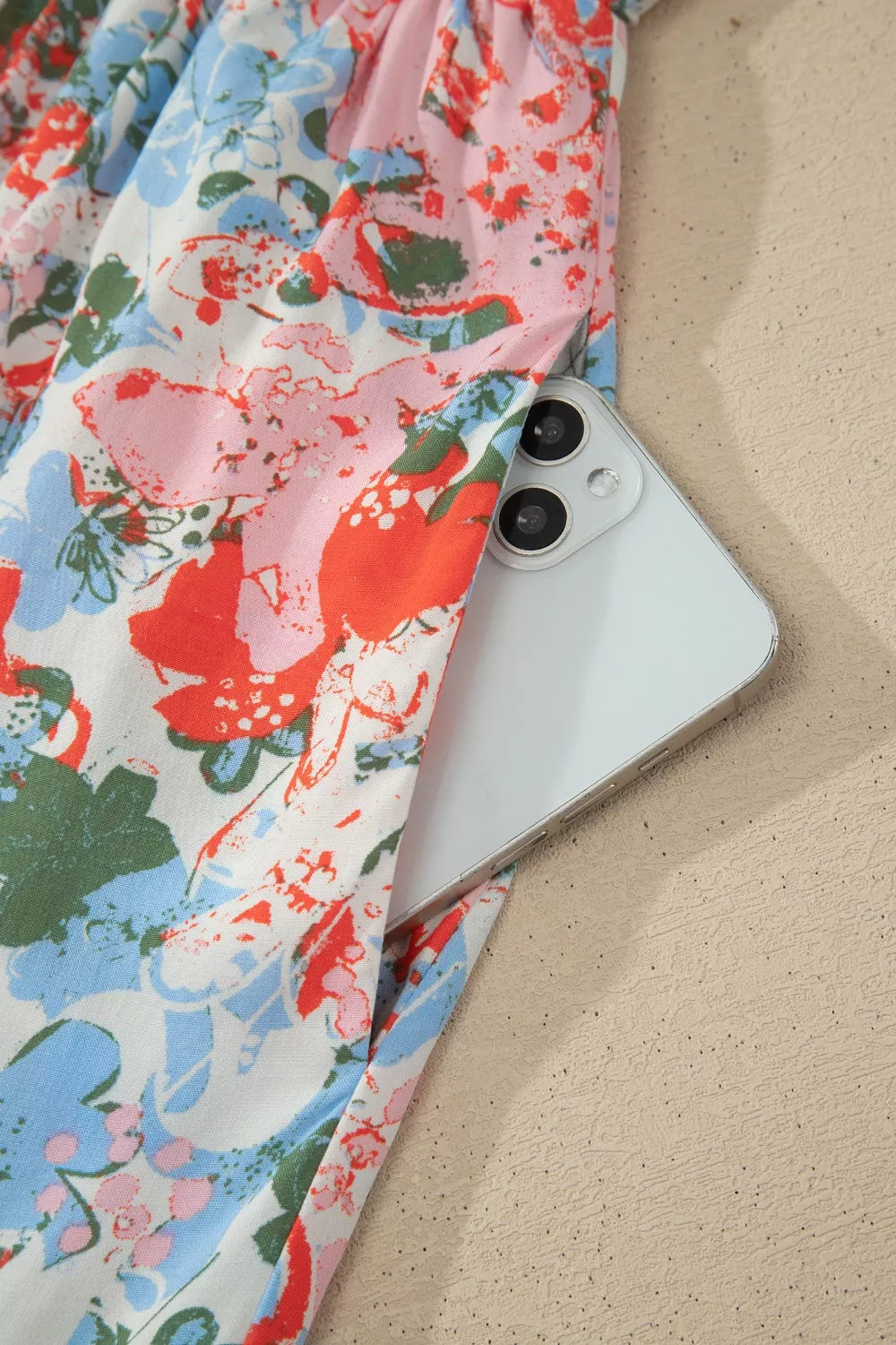 Vibrant floral maxi dress with flutter sleeves and side pocket detail, showing a phone.