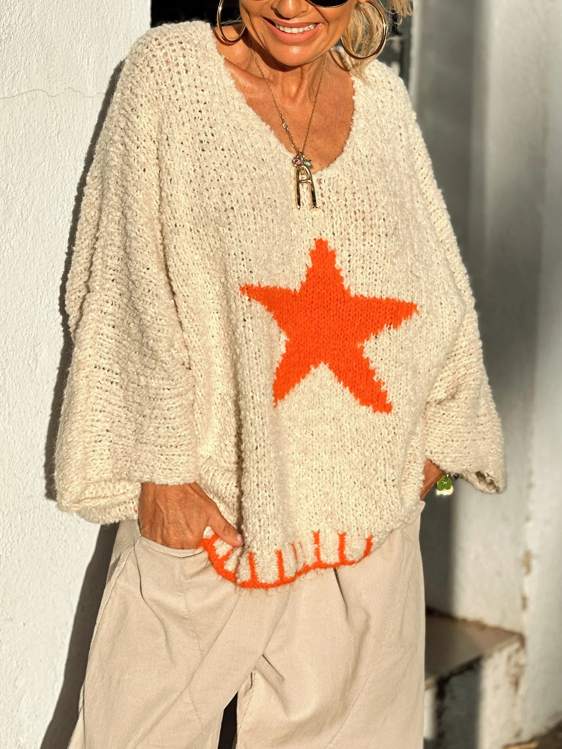 Cream knit v-neck sweater with orange star detail and ribbed hem.