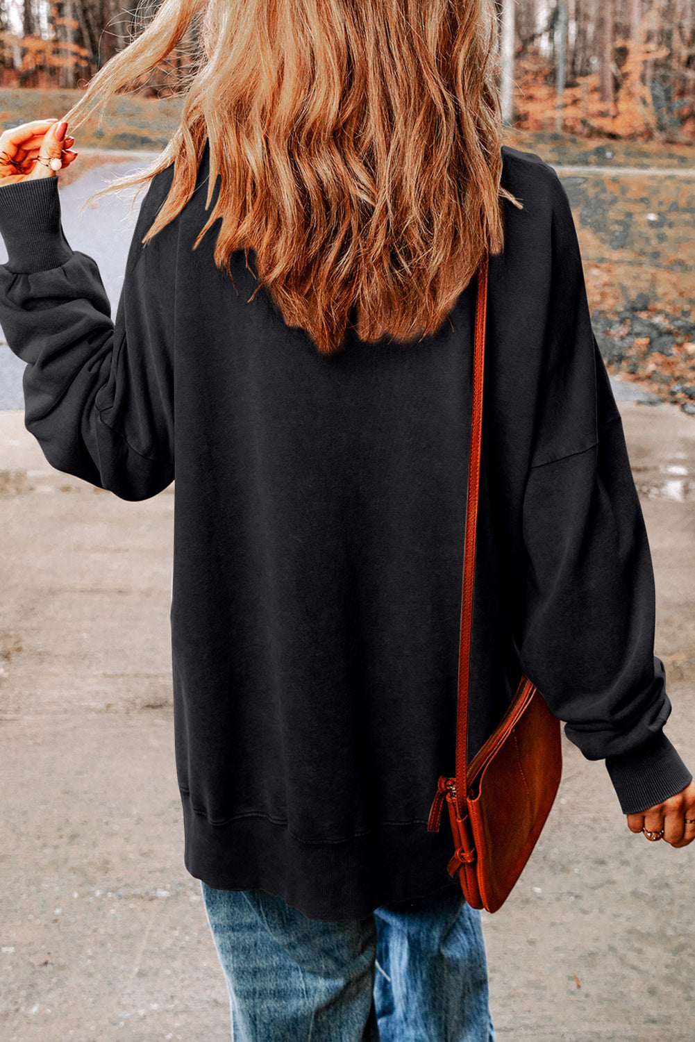 Black oversized graphic sweatshirt with crew neck and long sleeves, styled with jeans and a crossbody bag.