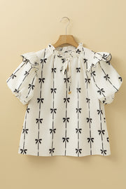 Ivory blouse with black bow print, ruffled neckline and sleeves, and tie detail.