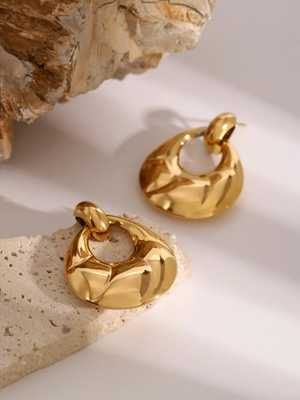 Gold statement earrings with sculpted, textured teardrop shape and open center.