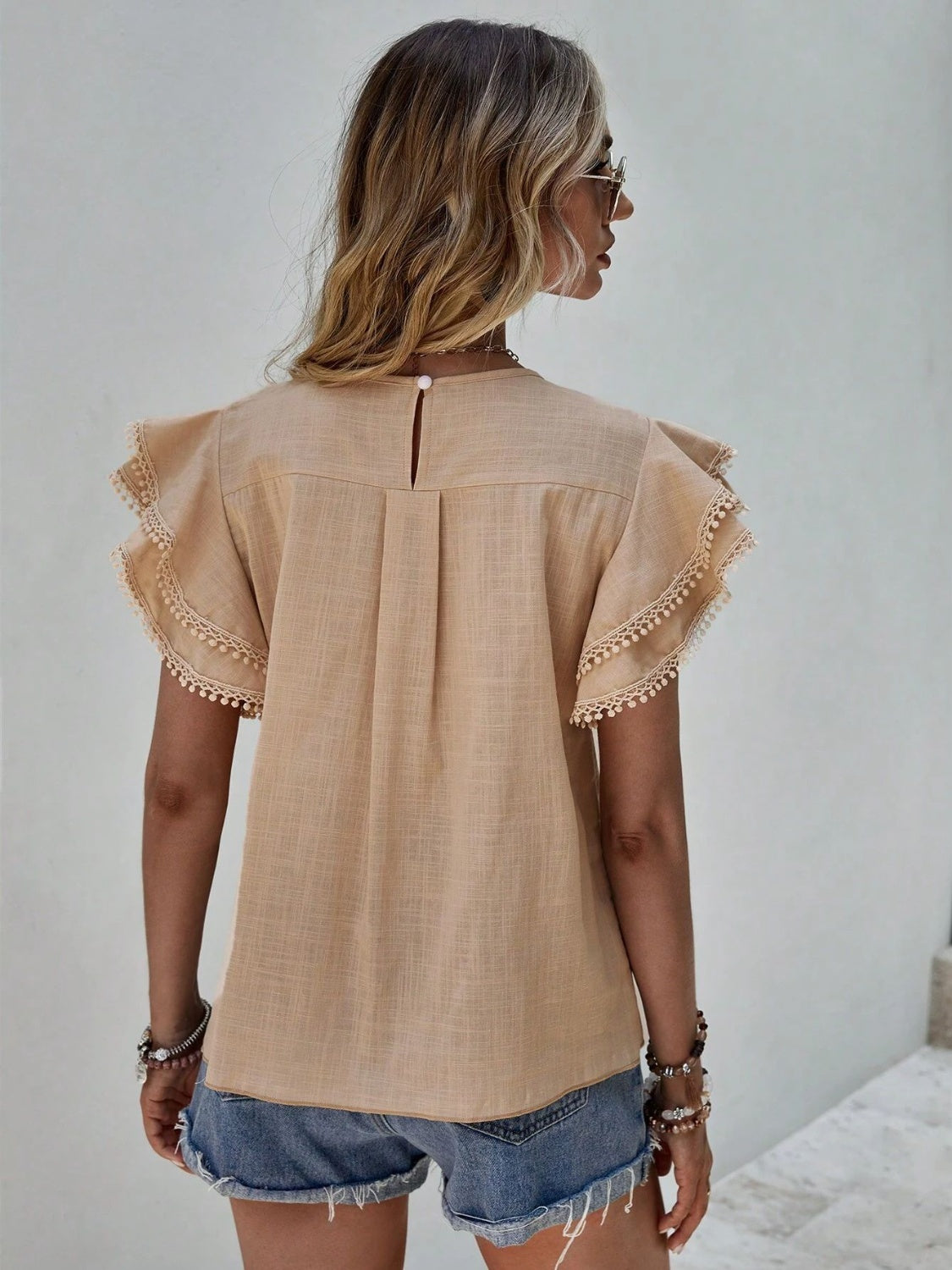 Khaki blouse with ruffle sleeves trimmed with pom-poms and a keyhole back detail.