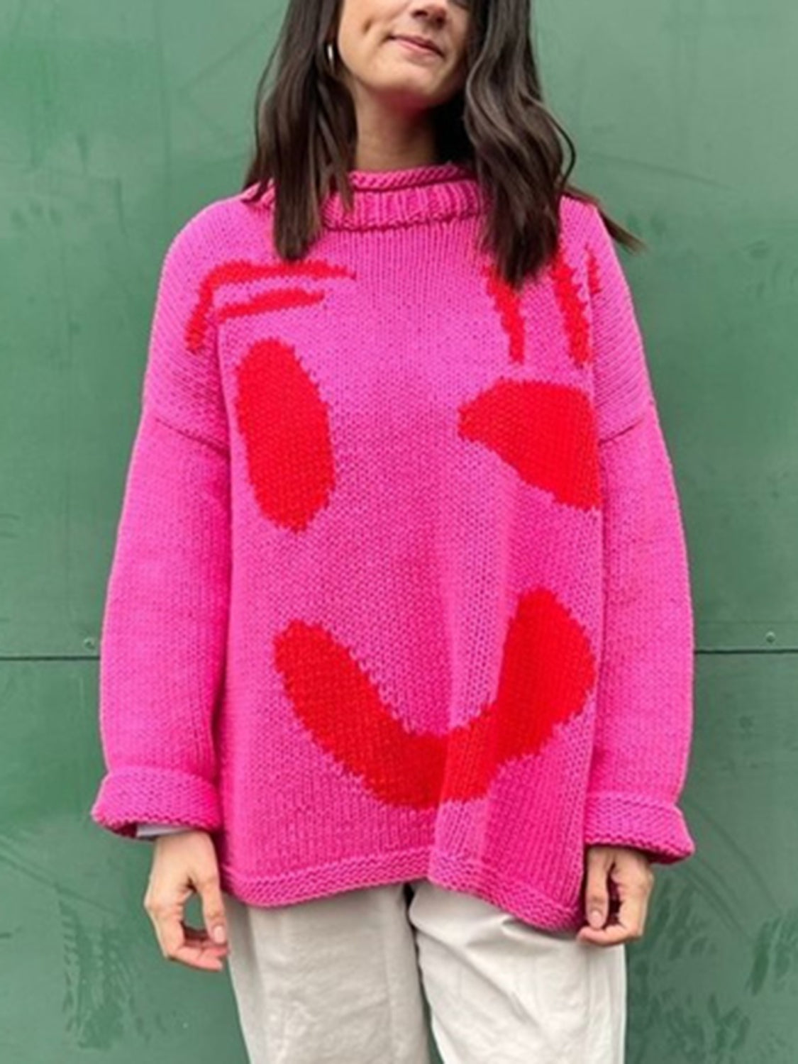 Hot pink knit sweater with abstract red graphic pattern, crew neck, and long sleeves.
