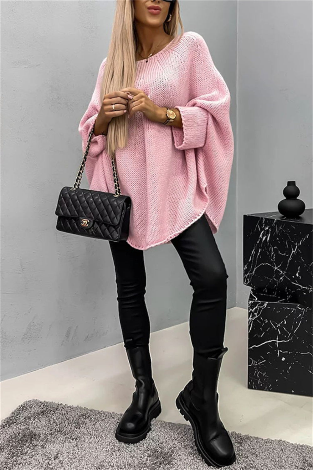 Blush pink knit sweater with cape sleeves and a relaxed fit, styled with black pants and boots.