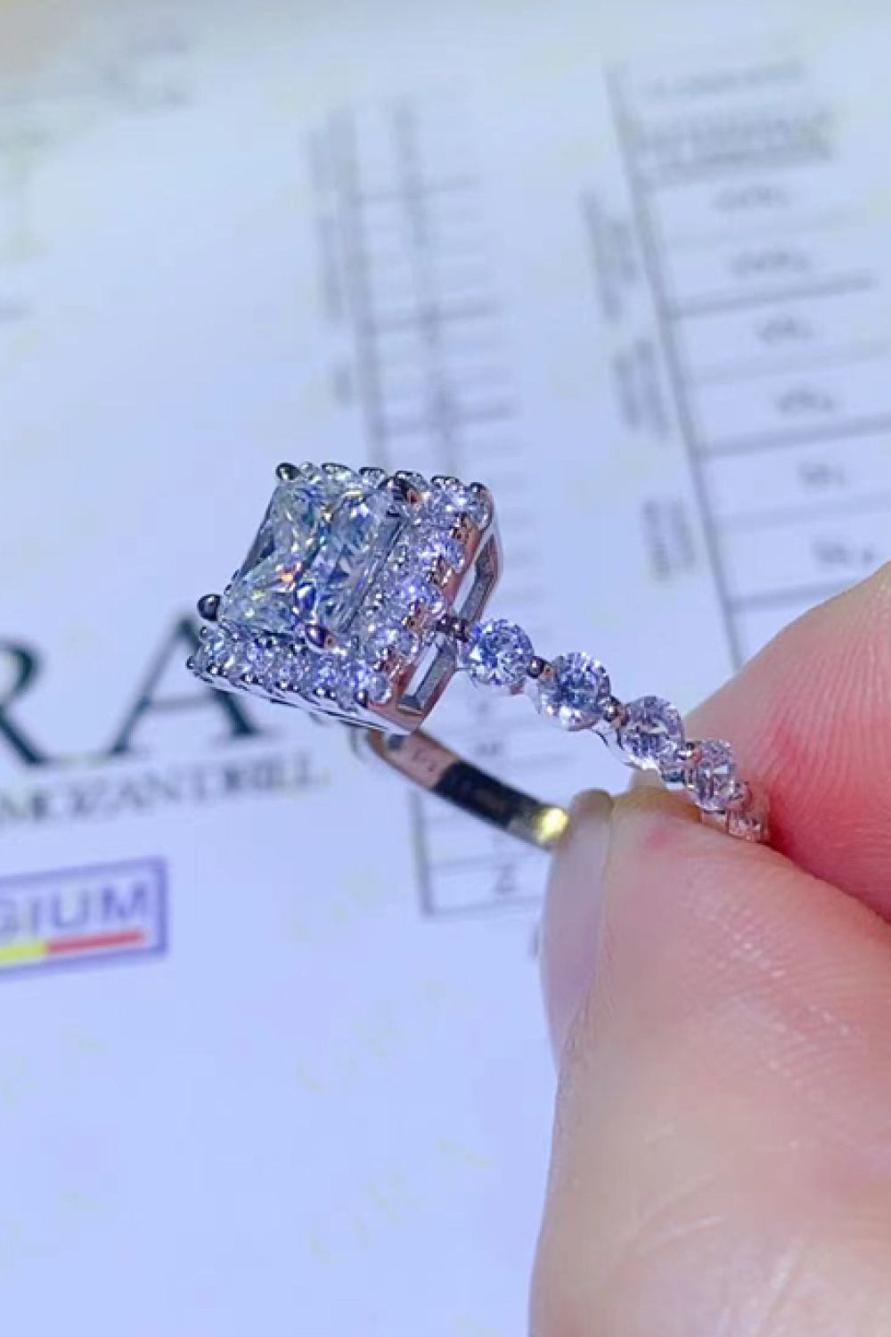 White moissanite engagement ring with cushion cut center stone and halo, set in white metal.