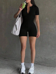 Black short-sleeve romper with zip front and cutout back detail, styled with white sneakers.