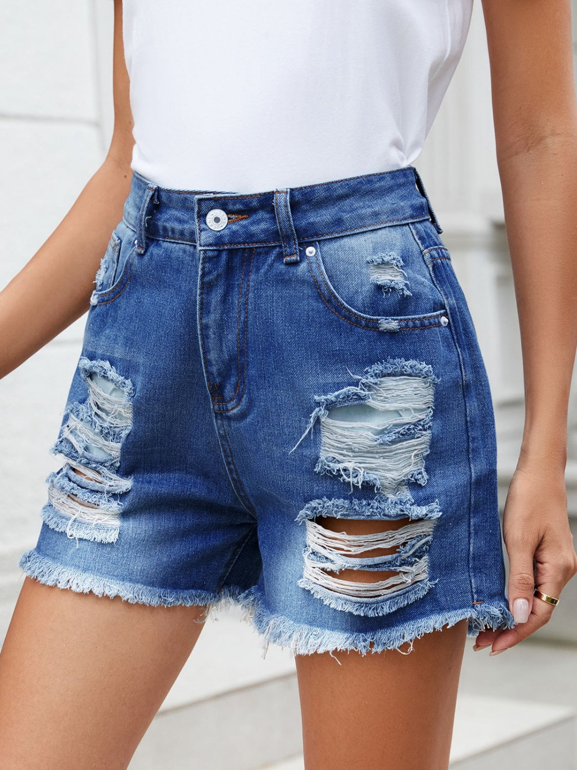 Medium wash denim shorts with distressed rips and raw hem