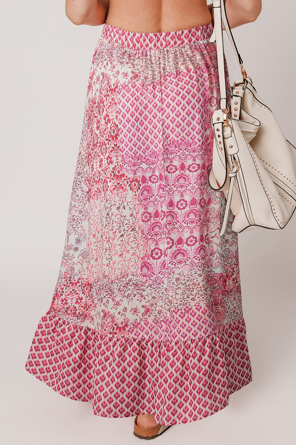 Printed tiered maxi skirt in dusty pink with boho patterns and a ruffled hem.