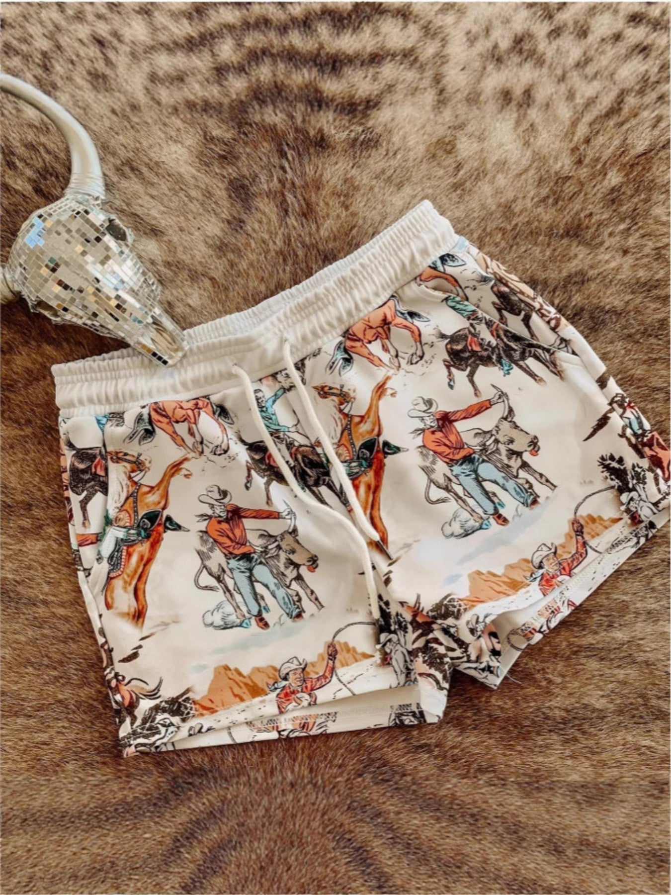 Rodeo print drawstring shorts with a white background and elastic waistband.