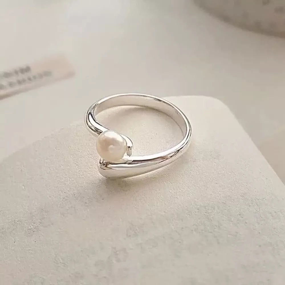 Silver bypass ring with a single luminous pearl accent.