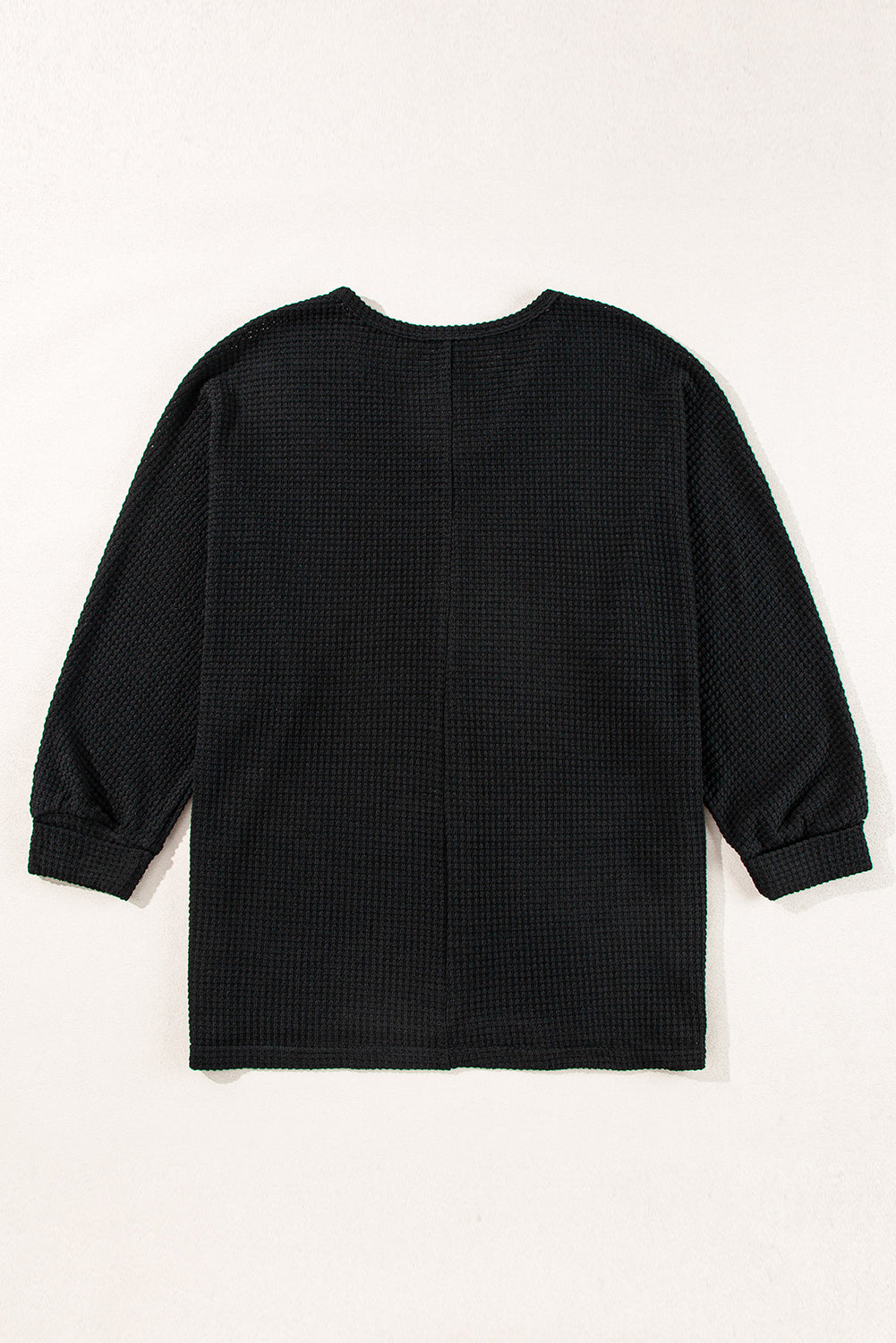 Black waffle knit V-neck top with long sleeves and a slit hem.