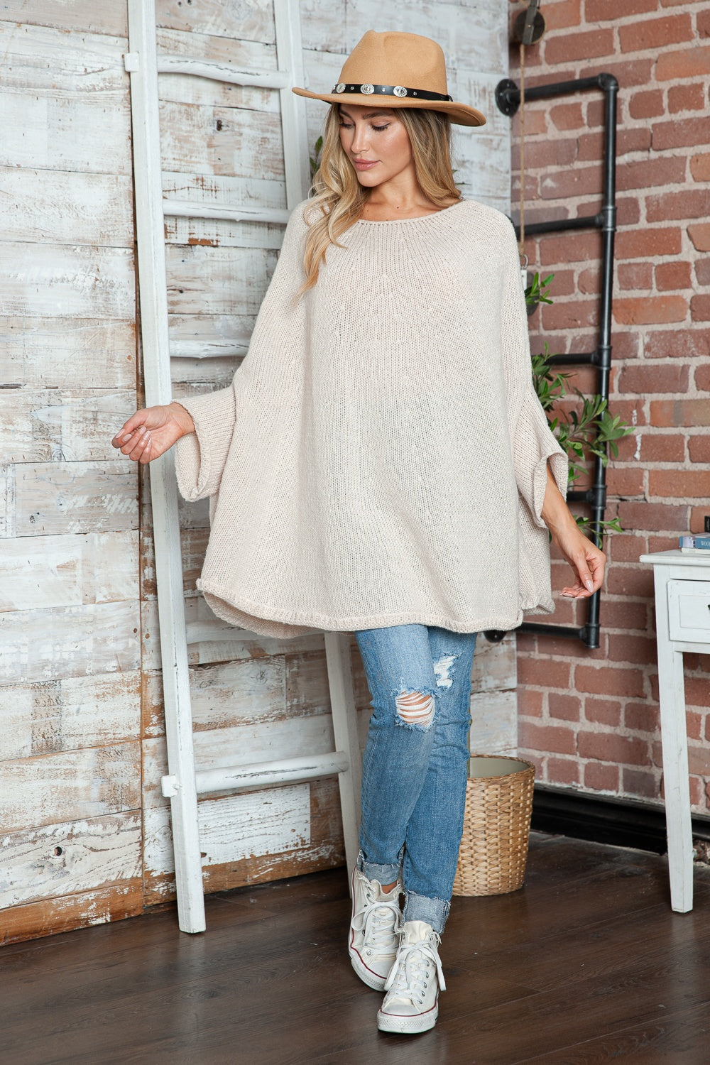 Cream knit cape sleeve sweater with wide sleeves, styled with ripped jeans and a hat.