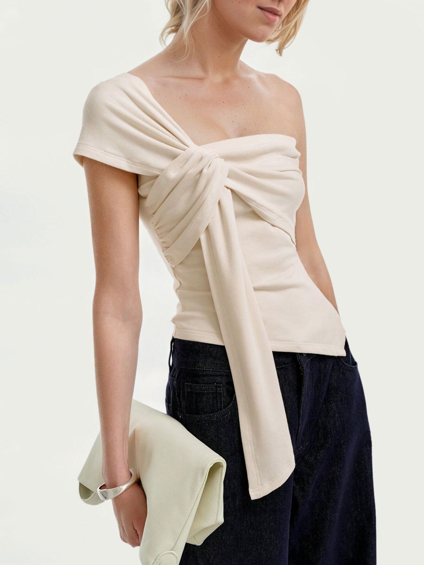 Beige asymmetrical t-shirt with knot detail and ruched sides, styled with dark denim.