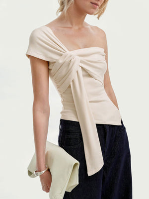 Beige asymmetrical t-shirt with knot detail and ruched sides, styled with dark denim.