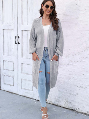 Charcoal ribbed knit maxi cardigan with pockets and balloon sleeves, worn open over a white top and ripped jeans.