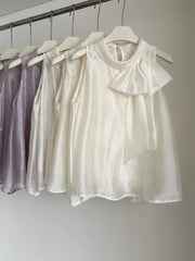 Sleeveless white shirt with a large bow detail and mock neck, available in purple and apricot.