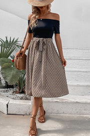 Black off-shoulder midi dress with a patterned A-line skirt and tie waist.