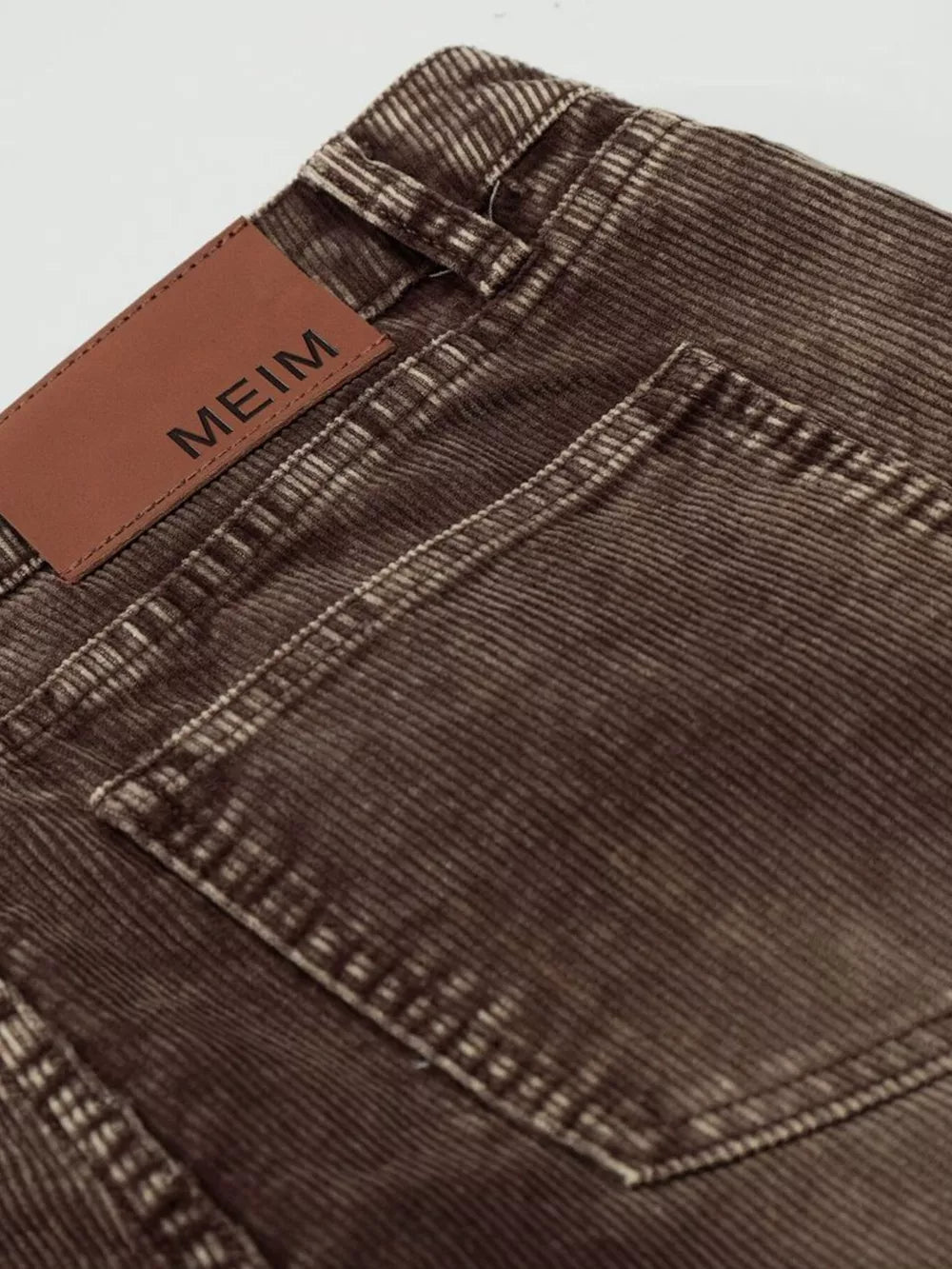 Brown corduroy joggers with a leather brand patch and visible stitching detail.