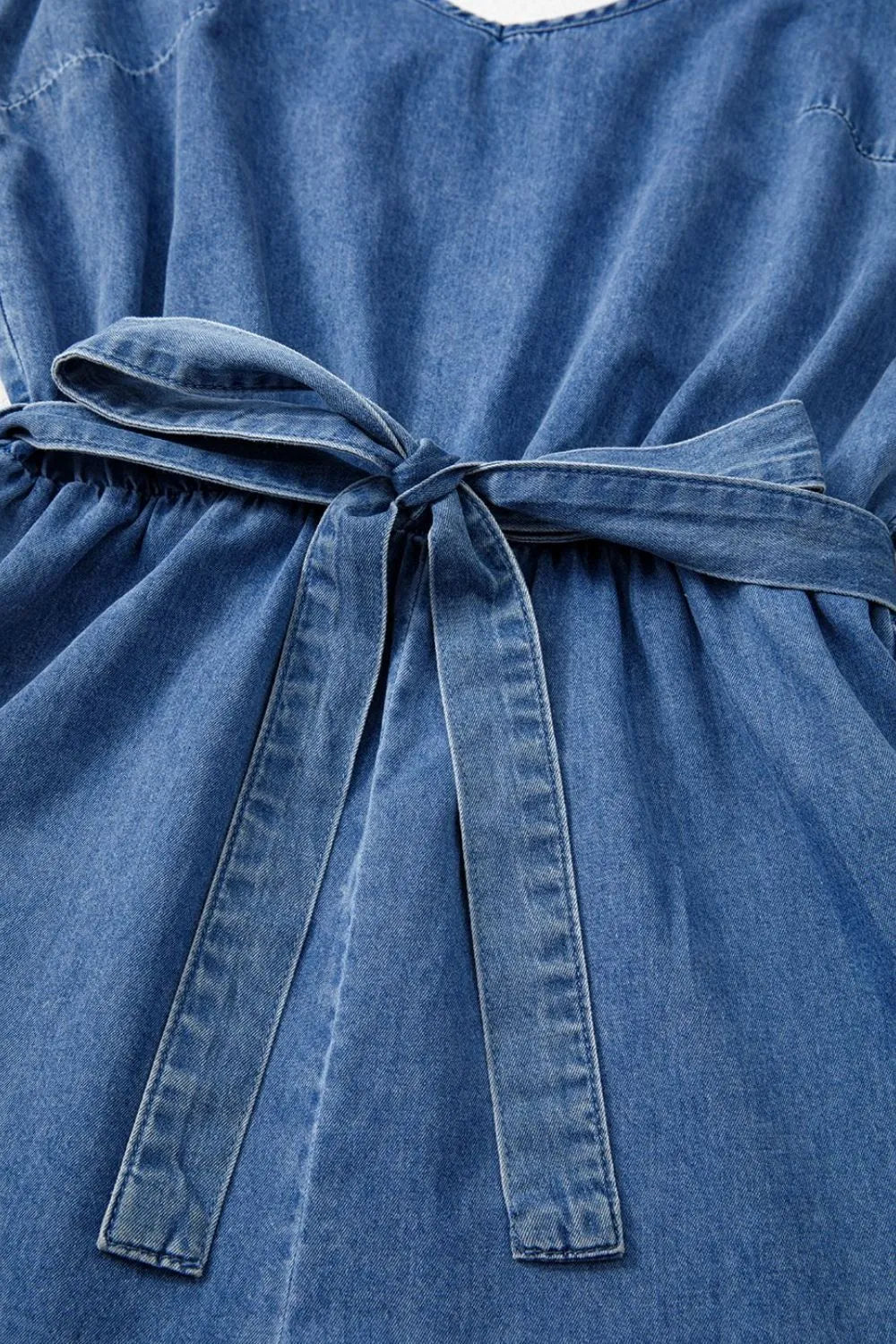 Medium wash denim romper with tie waist and ruffled hem detail