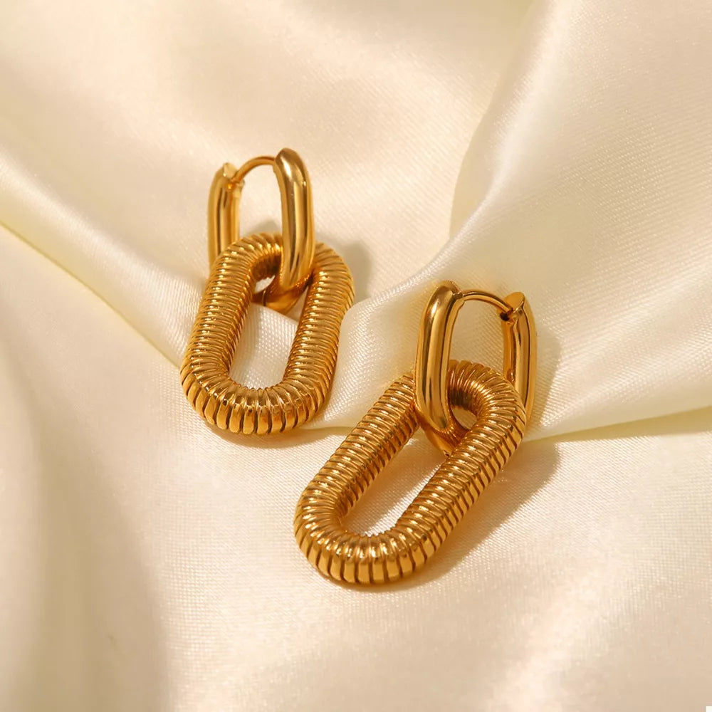 Gold link drop earrings with ribbed oval links on a satin background.