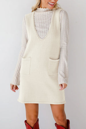 Sleeveless knit pocket dress in cream with V-neck, styled over a ribbed mock neck top.