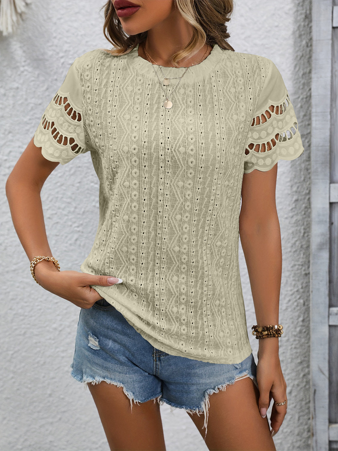 Beige eyelet blouse with scalloped short sleeves and intricate patterned fabric.