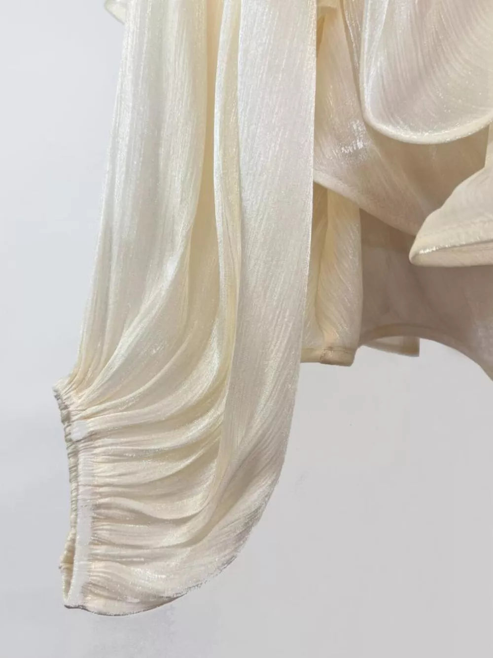 White ruffled mini dress with ruched sleeve detail and shimmering fabric.