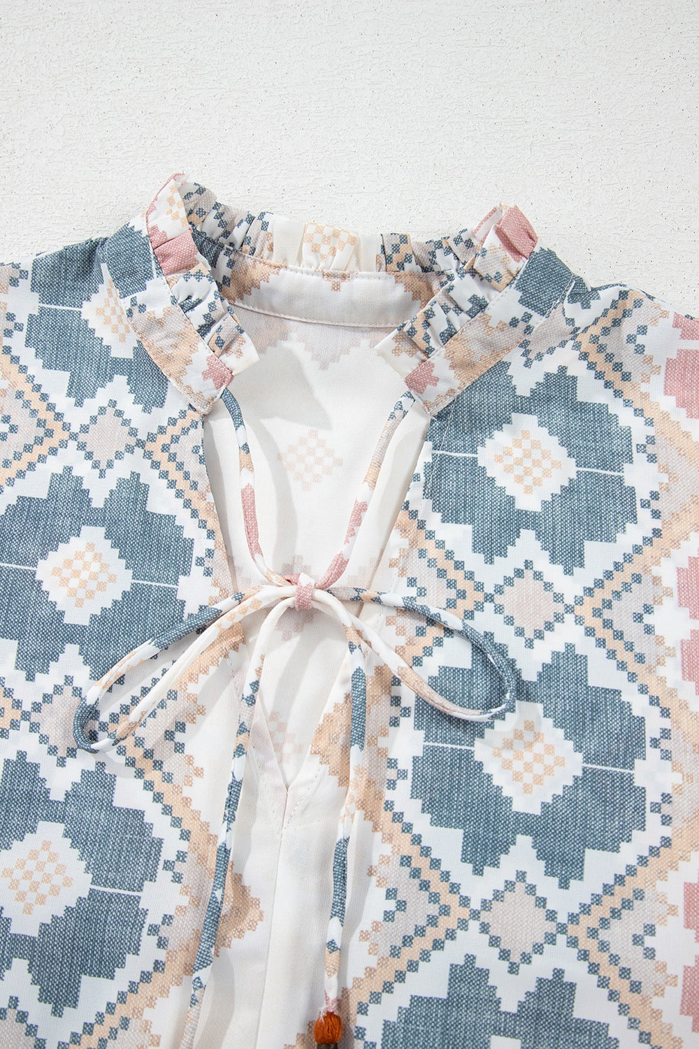 Geometric print blouse with ruffle neck and tassel tie detail in floral colors.