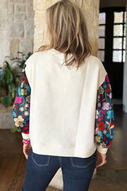 Ivory quilted knit top with colorful floral print sleeves.