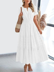 White tiered V-neck maxi dress with smocked waist and short sleeves, styled with sandals and a tote bag.