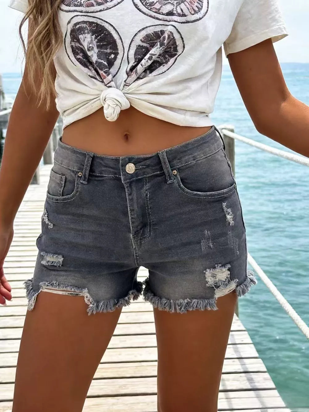 Gray distressed denim shorts with raw frayed hem and button fly.