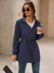 Navy hooded jacket with cinched waistline and zip front, styled with jeans.