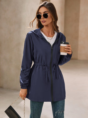 Navy hooded jacket with cinched waistline and zip front, styled with jeans.