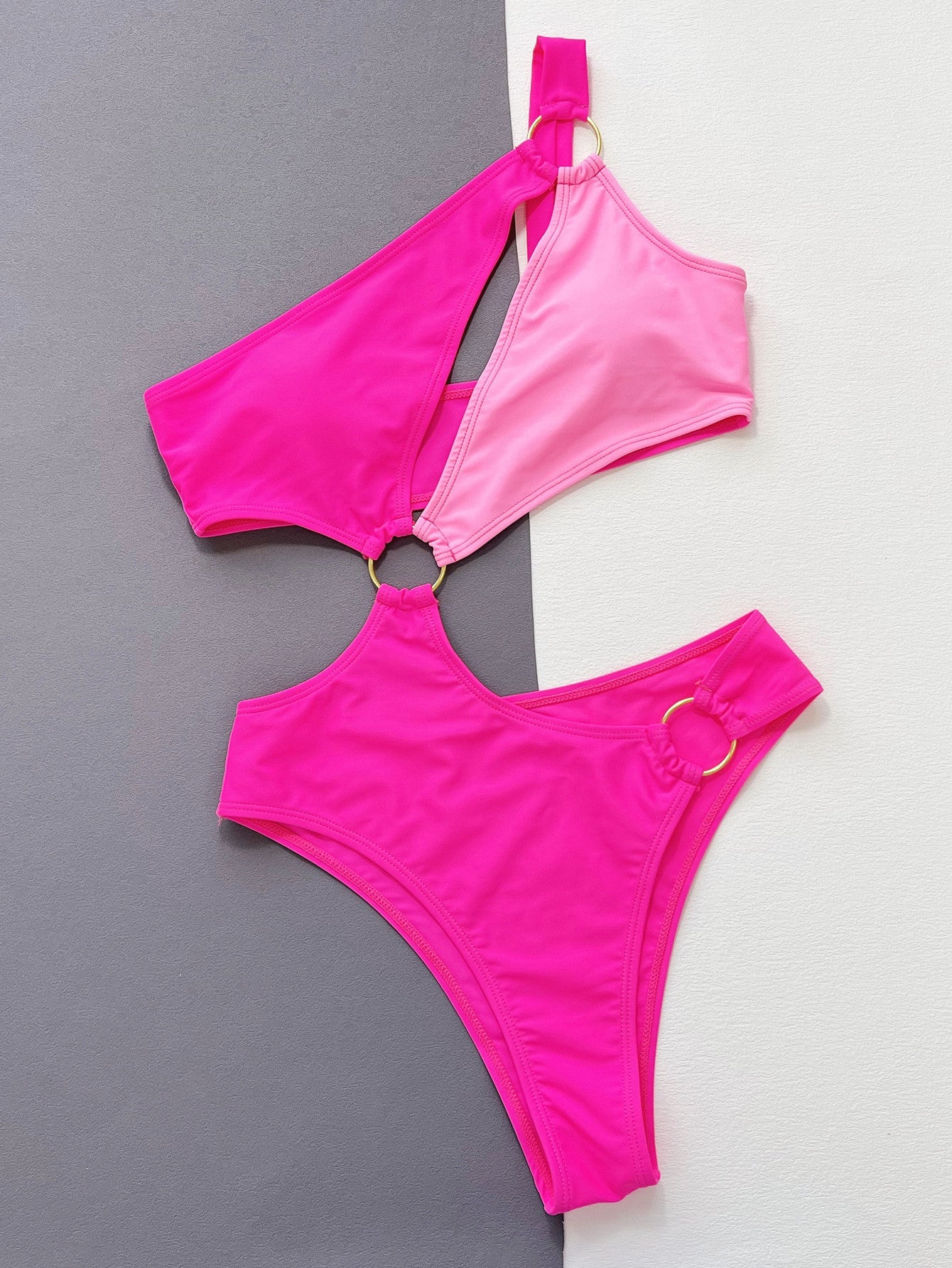 Hot pink one-piece swimsuit with asymmetric strap, cut-out detail, and gold ring accents.