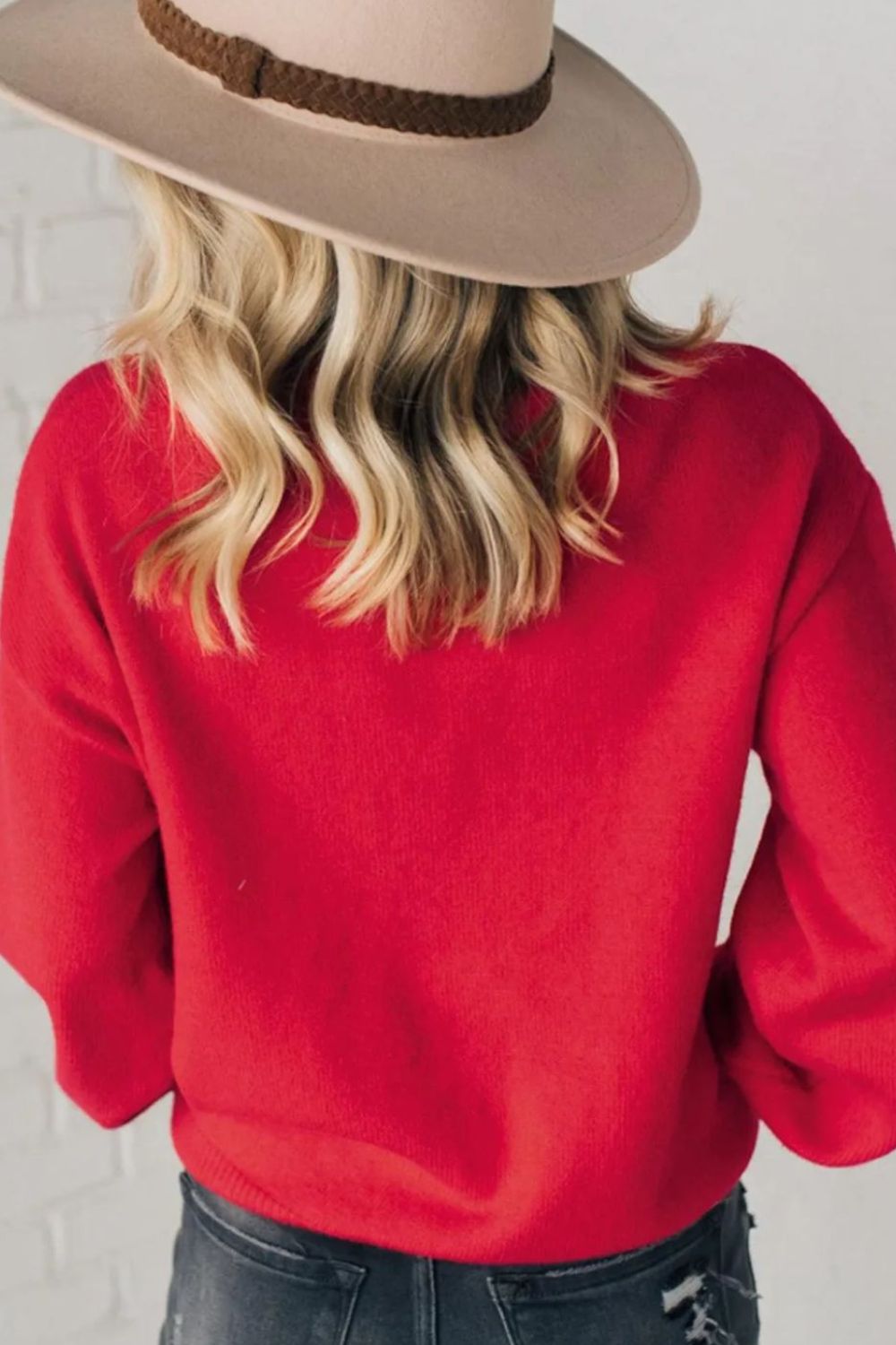Red knit sweater with pearl embellishments on the front, styled with a hat.