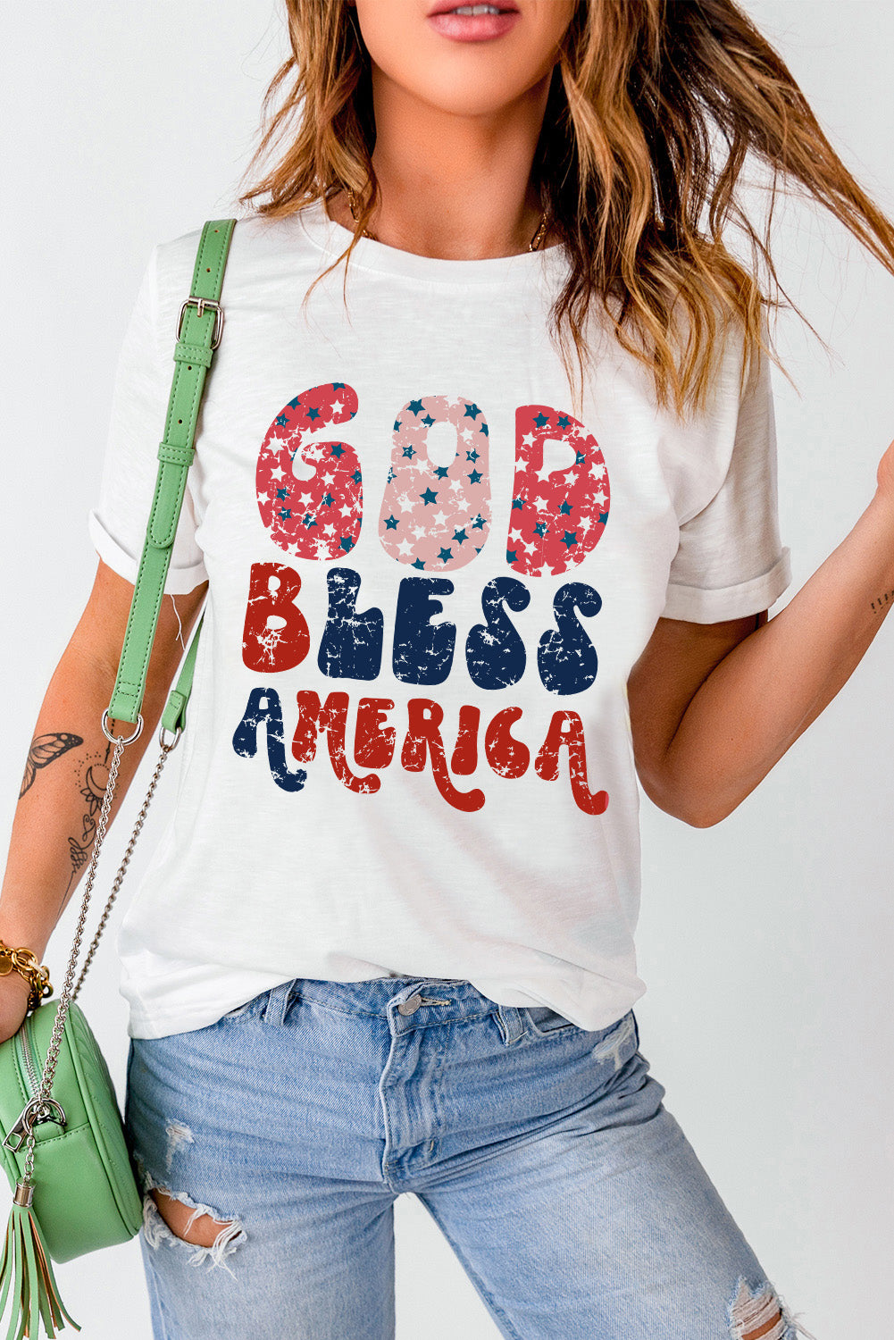 White graphic tee with distressed "God Bless America" text in red, white, and blue patriotic stars and stripes pattern.