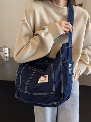Slouchy dark blue denim crossbody bag with contrast stitching and distressed detail.