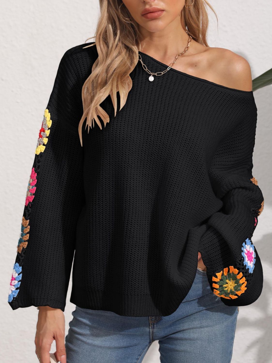 Black knit sweater with colorful granny square crochet sleeves, off-the-shoulder neckline.