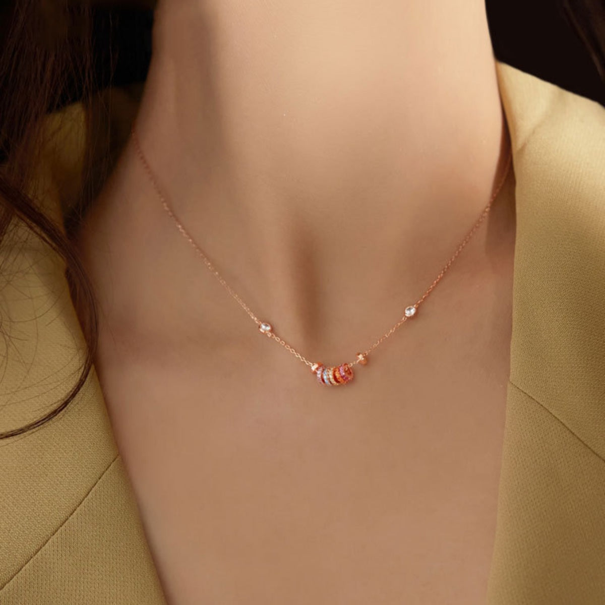 Rose gold necklace with a fine chain and a cluster of small, colorful rings and clear crystals.